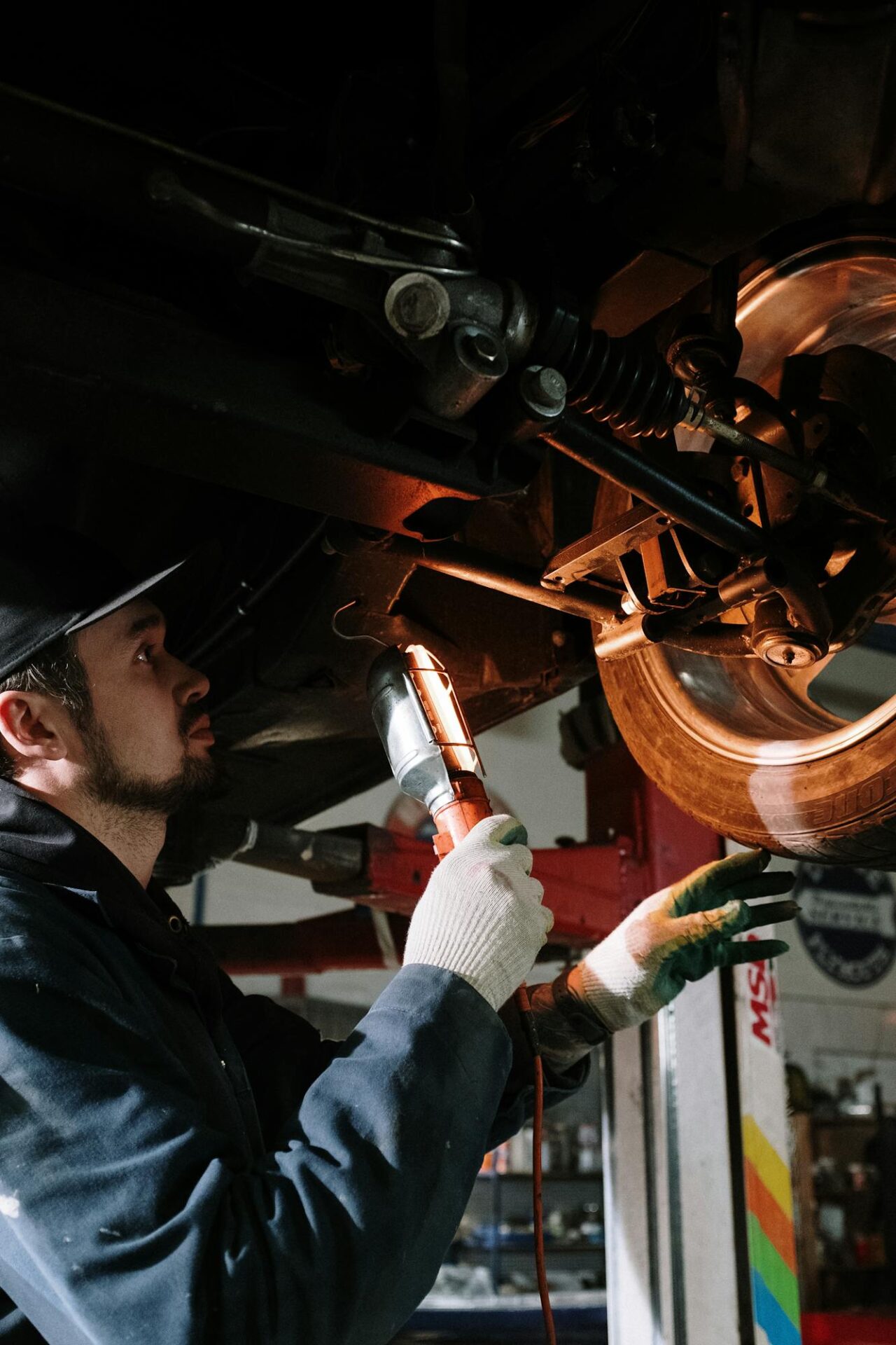 Mechanic inspecting rear wheel under car with flashlight for reno brake repair